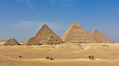 The famous Egyptian pyramids against a blue cloudy sky and tourists having a ride on camels