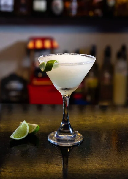A vertical shot of a glass of a blended margarita cocktail with lime on a table