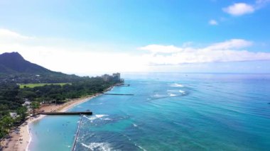 A drone shot of buildings and skyscrapers on a beautiful beach with crystal water under cloudy sky in Waikiki, Hawaii