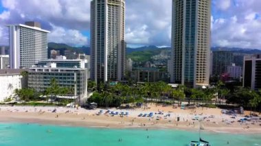 A drone shot of buildings and skyscrapers on a beautiful beach with crystal water under cloudy sky in Waikiki, Hawaii