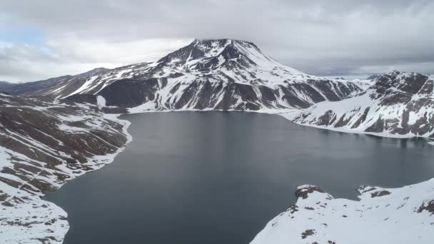 曇った日に雪に覆われた山々に囲まれた湖の空中ショット — ストック動画