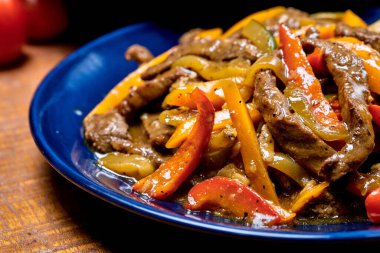 A closeup of fried beef with peppers on a blue plate