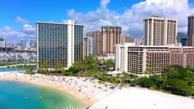 A drone shot of buildings and skyscrapers on a beautiful beach with crystal water under cloudy sky in Waikiki, Hawaii