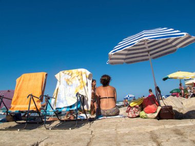 A back shot of a female sitting on a sandy beach on the sunny  beach in Mar del Plata, Argentina