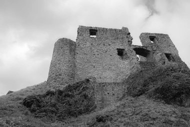A low angle shot of old castle ruins on top of a hill against a cloudy sky shot in grayscale