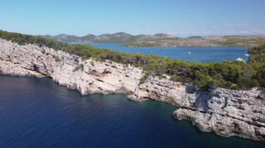 Footage of sea cliffs with bushes and mountain range in the background on a sunny day
