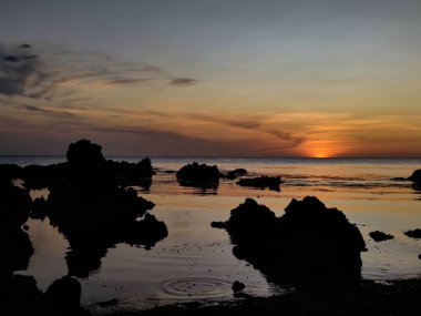 The silhouettes of the rocks near the shore against the background of the sea and sky at sunset.