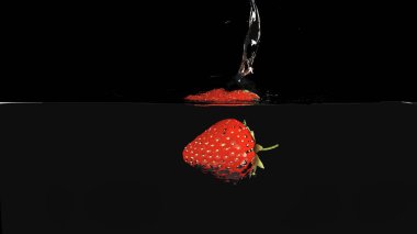 A red ripe strawberry falling into the water and splashing it on a black background