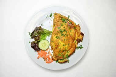 A top view of Omelette served with lettuce, vegetables, and chopped greens on a white plate on white table