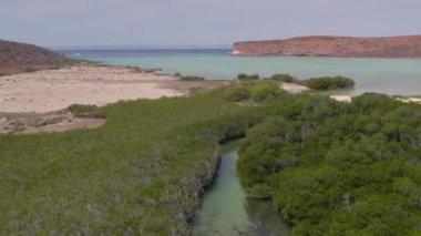 An aerial view of the wavy sea and the rocky mountains gleaming under the cloudy blue sky in 4K