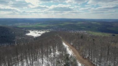 A bird's eye view of leafless forests covered with snow against green landscape in Bavaria, Germany