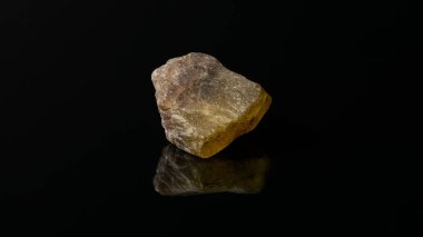 A closeup of an uncut and raw orange Meliphanite stone on a reflective black surface