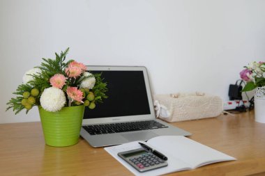 A vase with a beautiful bouquet on a working desk with a laptop and a notebook