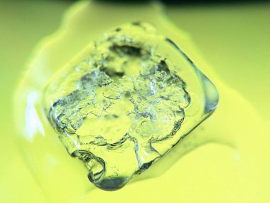 A vertical closeup of an ice cube melting on a green background
