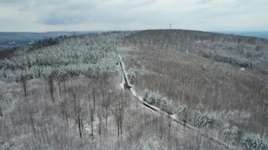 An aerial shot of a road surrounded by leafless forests covered with snow in winter in Bavaria,Germany