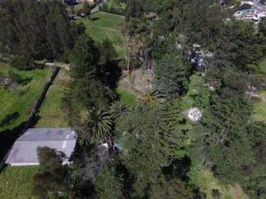 Güneşli bir günde yeşil ormanlarla kaplı tepelerin ve kırsal alandaki evlerin kuş bakışı görüntüsü