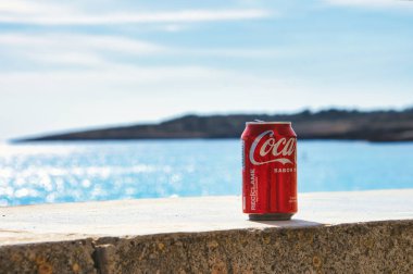 Picture shows a Coca Cola can on a brick wall in Cala Millor, Mallorca. The Mediterranean Sea and a headland in the background.