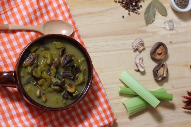 A top view of a delicious bowl of green mushroom and celery   broth on a rustic kitchen table