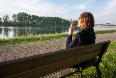 Yetişkin bir kadın bacak bacak bacak üstüne atmış sigara içiyor baharda göl kenarında bir bankta oturuyor.