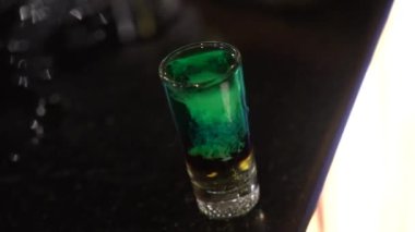 A person mixing alcoholic drink in shot glass on the bar table