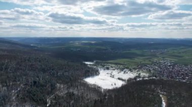 A bird's eye view of leafless forests covered with snow against green landscape in Bavaria, Germany