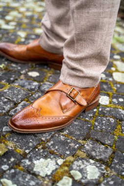 A vertical closeup of men's brown oxford shoes on feet outdoors