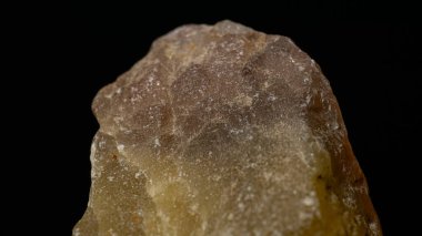 Kesilmemiş ve çiğ turuncu bir Meliphanite taşına yakın plan. Siyah arka planda izole edilmiş.