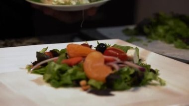 A professional chef adding feta cheese on a salad with tomatoes, onions, greens and mandarins