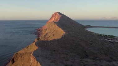 An aerial view of the wavy sea and the rocky mountains gleaming under the cloudy blue sky in 4K