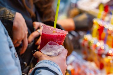 Unrecognizable girl holding a glass of strawberry juice in the market, selective focus on the glass.