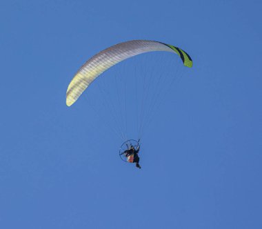 A low angle shot of a person paragliding in a blue cloudless sky on a sunny day