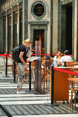 A vertical shot of a female tourist reading the menu at a restaurant terrace in Turin, Italy.