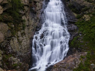 A beautiful long exposure shot of a natural waterfall dropping on big rocky mountain