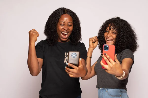 African Nigerian Excited Girls Checking Phones Isolated Background — Stock Photo, Image