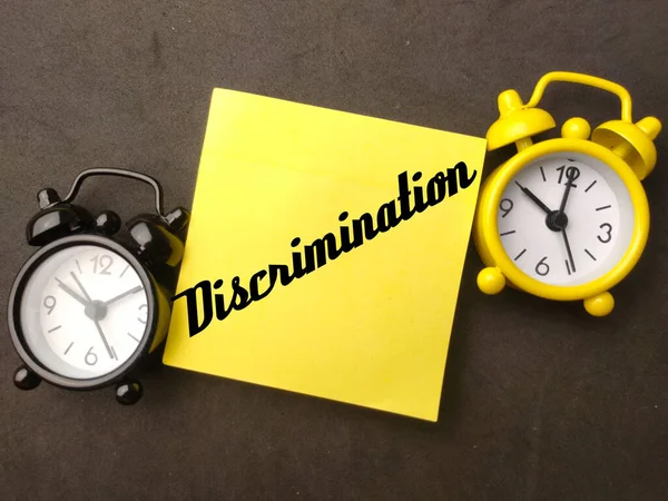 The two alarm clocks and a sticky note with the word Discrimination