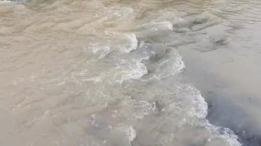 A beautiful view of a river with brown water flowing on stones and rocks in bright sunlight