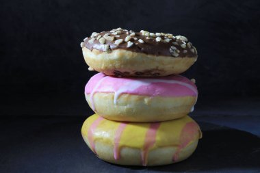 Koyu arkaplanda bir sütundaki çeşitli renkli çörekleri kapat