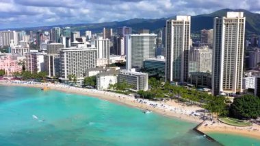 A drone shot of buildings and skyscrapers on a beautiful beach with crystal water under cloudy sky in Waikiki, Hawaii