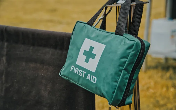Green First Aid Bag with black straps hanging on a silver metal pole on a summers day at a barbeque