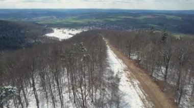 A bird's eye view of leafless forests covered with snow against green landscape in Bavaria, Germany