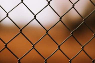 A closeup of a metallic net fence against a blurry brown background