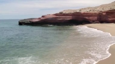 An aerial view of the wavy sea and the rocky mountains gleaming under the cloudy blue sky in 4K