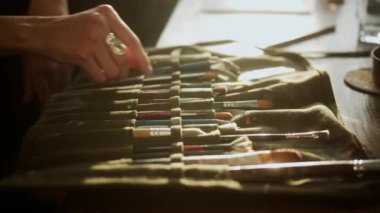 A closeup shot of a female hand taking a painting brush from a pack on a wooden table indoor in daylight