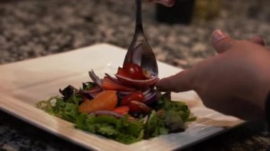 Profesyonel bir aşçı beyaz tabakta salata yeşilliklerine domates, soğan ve mandalina ekliyor.