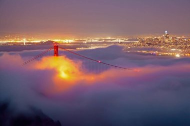 Sisli bir günde, arka planda güzel gece ışıkları olan Golden Gate Köprüsü 'nün nefes kesici bir görüntüsü.