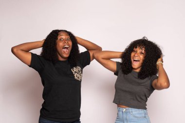 Gülen iki Afrikalı kız, izole edilmiş arka planda dokunarak mutlu ve heyecanlı.