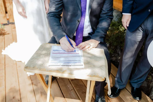 Closeup Shot Groom Signing Wedding Contract Papers Wooden Table Sunny — Stock Photo, Image