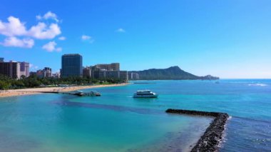 Waikiki, Hawaii 'de bulutlu gökyüzünün altında kristal sularda seyreden güzel bir sahilde binaların ve gökdelenlerin insansız hava aracı görüntüsü.