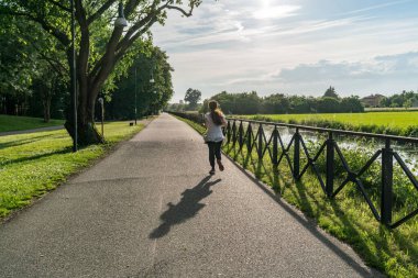 Güneşli bir baharda, İtalya 'nın Milano şehrinde akan bir nehir olan Naviglio della Martesana boyunca koşan bir kız.