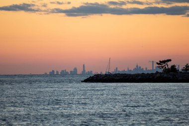 Okyanus üzerinde nefes kesici bir gün batımı manzarası. Arka planda New York şehrinin silueti var.